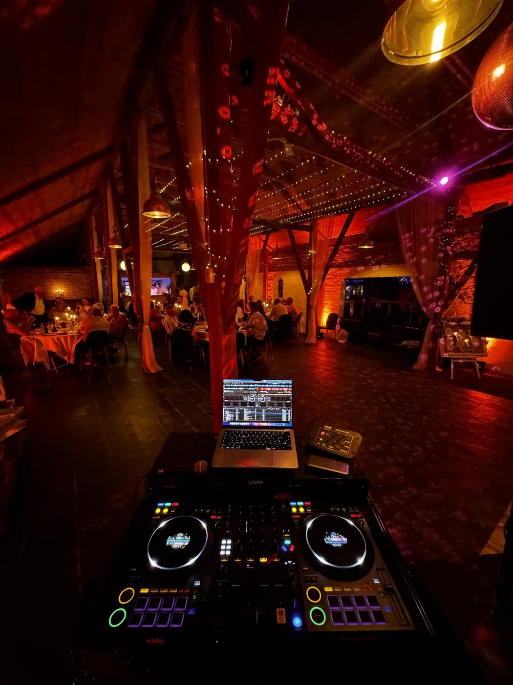 DJ-controller og laptop foran en fest i en lade med lyskæder